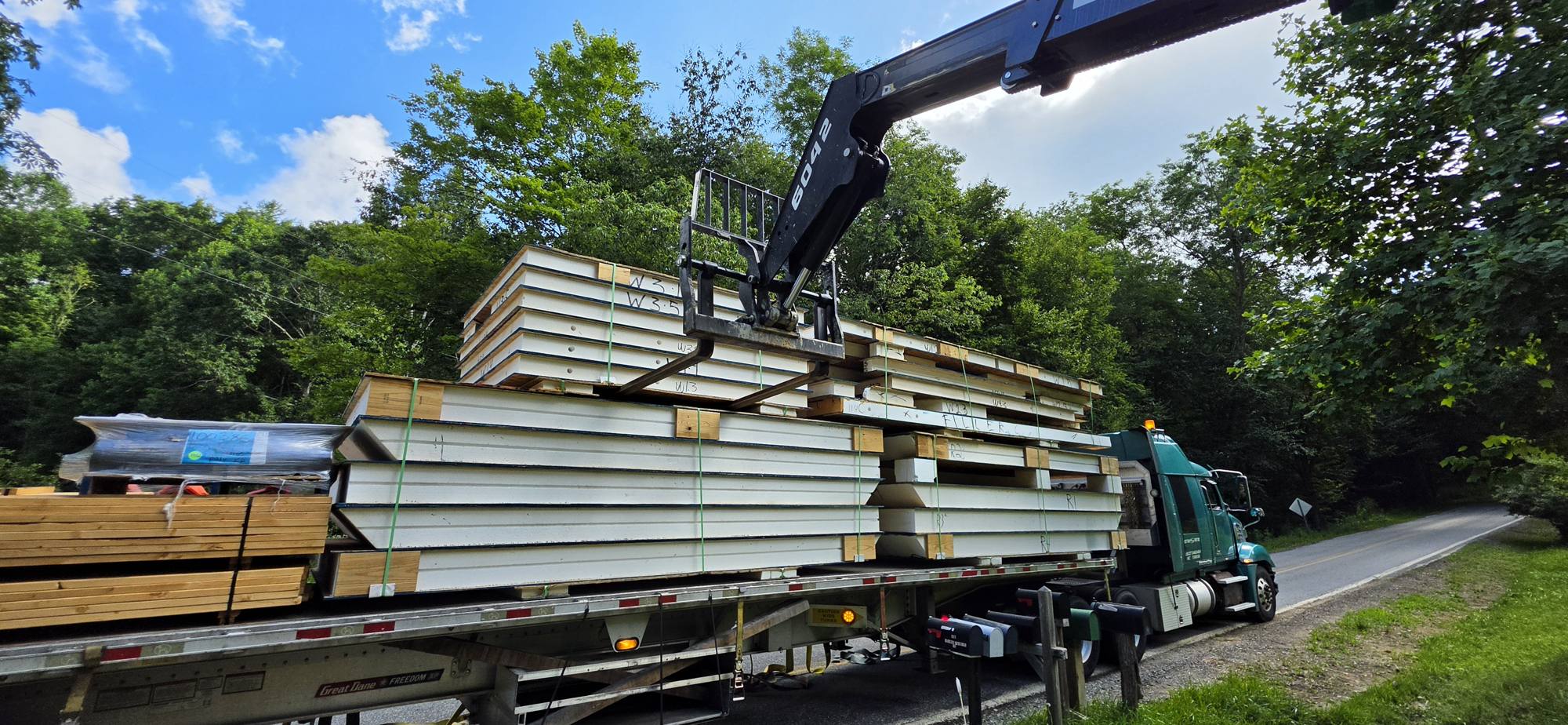 Truck-mounted crane lifting a stack of SIP panels off the trailer