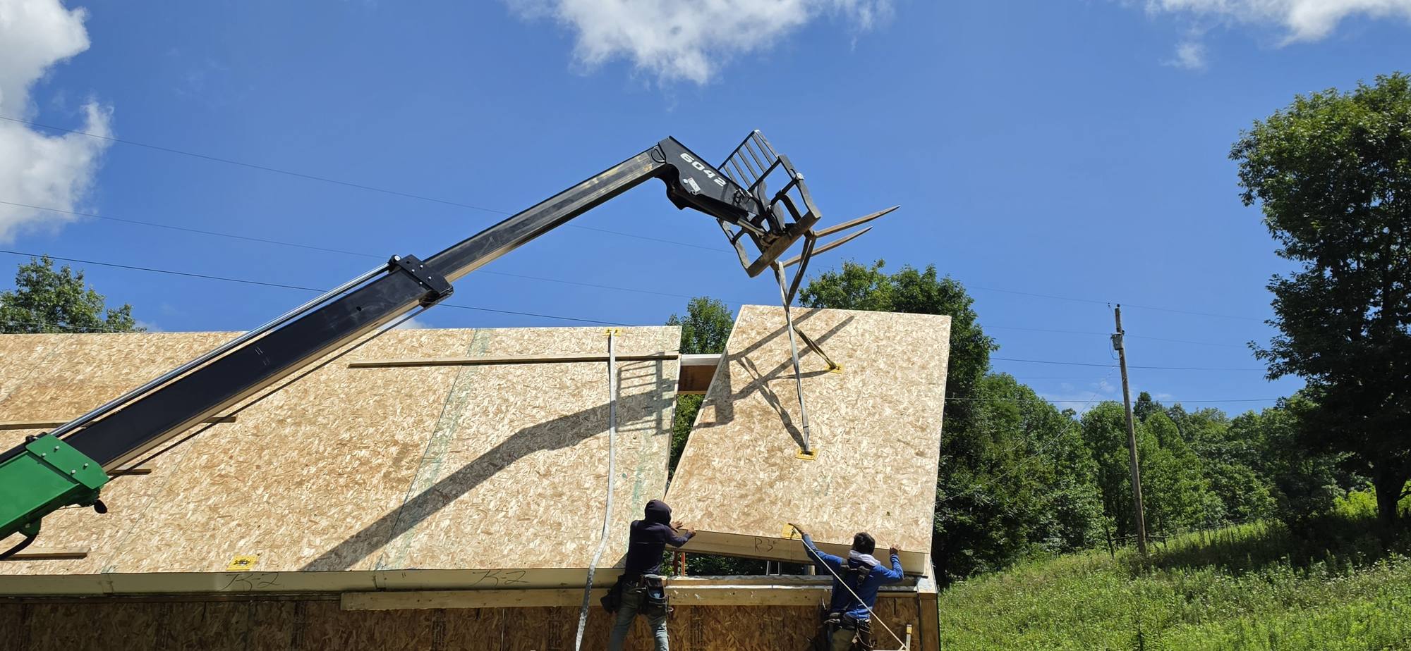 Crew setting SIP roof panels from a telehandler